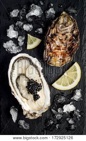 Oysters with black sturgeon caviar and lemon on black slate stone background. Top view flat lay