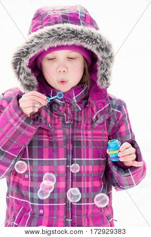Little girl playing outdoors in snow blowing bubbles