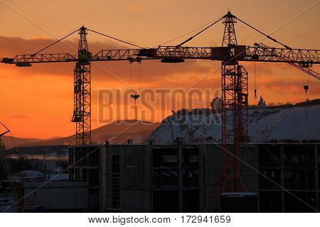 Construction crane on the orange sunset landscape.
