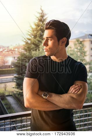 Profile of handsome attractive young man outdoor, looking to a side. Half-body shot, with arms crossed on chest