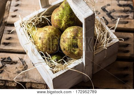 Heap of ripe organic conference pears in weathered wood box in straw natural light kinfolk style top view