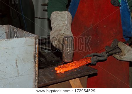 Red hot from the intense heat of a forge the blacksmith skillfully works the glowing metal to contour it into a handmade knife.
