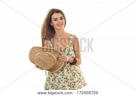 cheerful brunette woman in sarafan with floral patter and straw hat posing and smiling on camera isolated on white