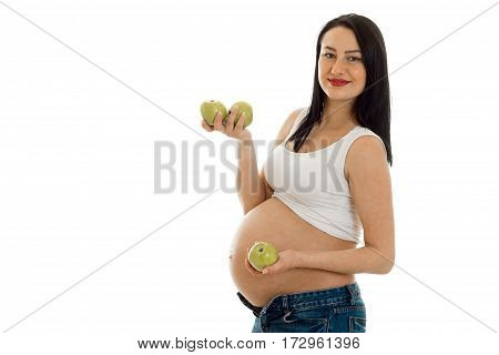 pregnant cheerful brunette woman with big belly and green apples in her hands looking on camera isolated on white