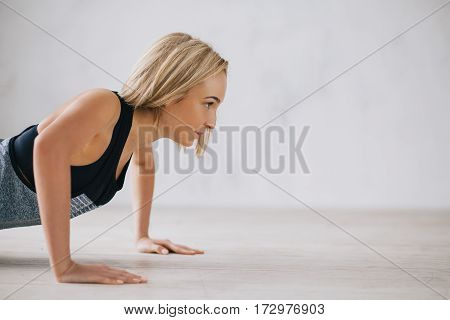 Closeup of young happy attractive woman doing push ups or press ups exercise. Serious girl trying to work out hard. White background