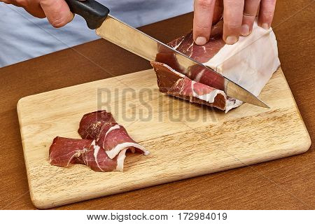 Dry cured ham thinly sliced Closeup on chef hands slices prosciutto Italian delicatessen dishes cooking process