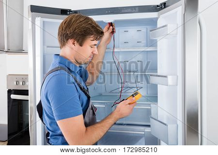 Male Technician In Overall Checking Refrigerator With Multimeter At Home