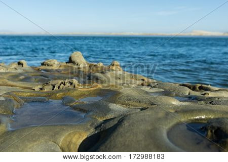 Unusual geological rock formations on estuary at base of cliff at Mangawhai Heads with de-focused sea and horizon background