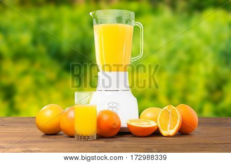 Fresh orange fruit and glass of orange juice or smoothies refreshment drinking on wooden rustic table in green garden background with blender. Healthy food. Tasty drink. Ecological environment