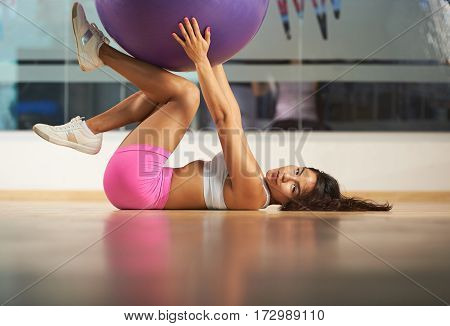Young woman laying on fitness club flooor and hold fitball. Hispanic girl with fitball