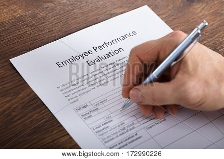 High Angle View Of A Person Filling A Performance Evaluation Form Of Employee