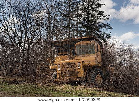 Rusting and overgrown heavy yellow industrial truck and equipment abandoned in economic recession
