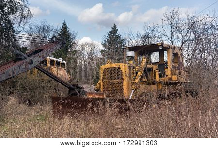 Rusting and overgrown heavy yellow industrial truck and equipment abandoned in economic recession