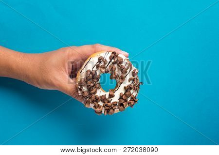 Hand Holding Delicious Glazed Doughnuts With Choclate Cereal Topping On Color Background