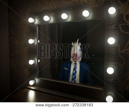 Glamour Guy In Suit And Mask Looks At Himself In The Mirror In Dressing Room. Freaky Young Man In St