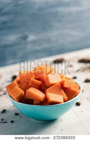 closeup of a pile of chopped raw pumpkin in a pale green bowl placed on a wooden table