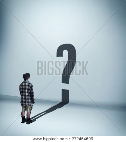 Man Standing In Front Of Wall And His Shadow Is Shaped As A Question Mark.
