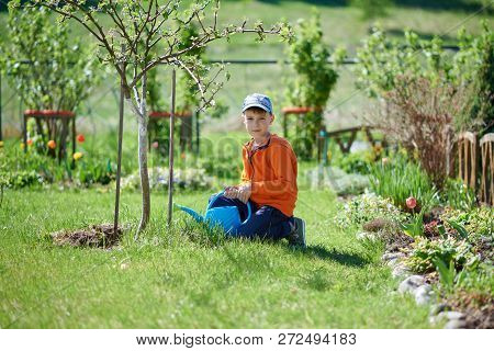 Cute European Boy Is Helping His Parents In The Countryside Croft. He Is Sitting Under The Tree In T