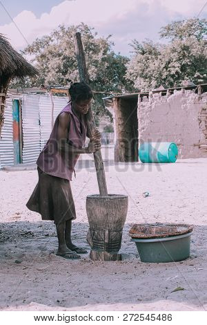 Namibia, Mbeyo, May 12: An Unidentified Dirty And Poor Woman Crushing The Millet In Mortar Near Town