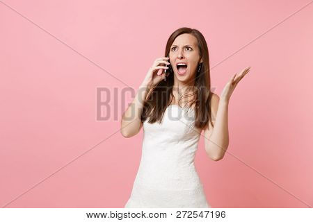 Angry Irritated Bride Woman In White Wedding Dress Spreading Hands, Talking On Mobile Phone, Screami