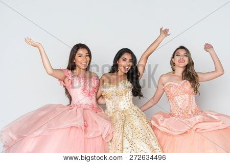 Group of three teenage hispanic girls wearing quinceanera dresses