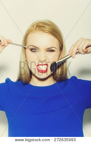 Woman Winking And Angry With Makeup Brushes. Funny Woman With Long Blond Hair In Blue Dress On White