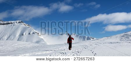 Skier With Skis On His Shoulder Go Up To Top Of Mountain In Nice Sun Day. Caucasus Mountains In Wint