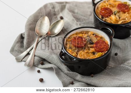 Slovak Christmas National Cabbage Soup In Two Small Black Pots With Sausage On The Tablecloth Backgr