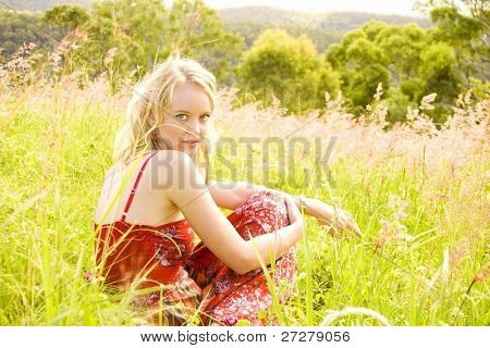 mooi meisje zit in een gras veld in de middag zon