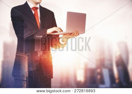 Unrecognizable Businessman Wearing Suit And Red Tie And Holding Laptop Standing Over Blurred Citysca