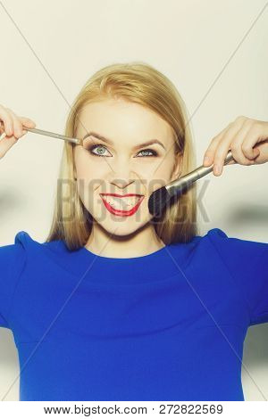 Girl Winking And Smiling With Makeup Brushes. Funny Woman With Long Blond Hair In Blue Dress On Whit