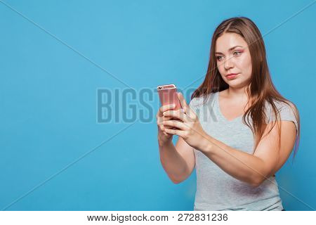 Young Attractive Caucasian Woman With Brown Hair And Bright Blue Eyes Looks To The Pink Mobile Phone