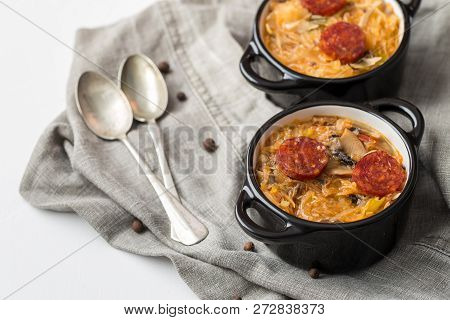 Slovak Christmas National Cabbage Soup In Two Small Black Pots With Sausage On The Tablecloth Backgr