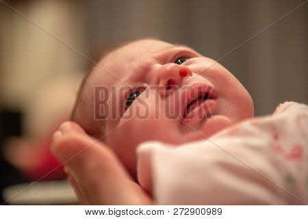 Infant Held In Hands View From The Bottom. Neutral Or Slightly Unhappy Face Expression.