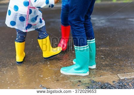 Close-up Of Three Children, Toddler Girl And Two Kids Boys Wearing Red, Yellow And Green Rain Boots 