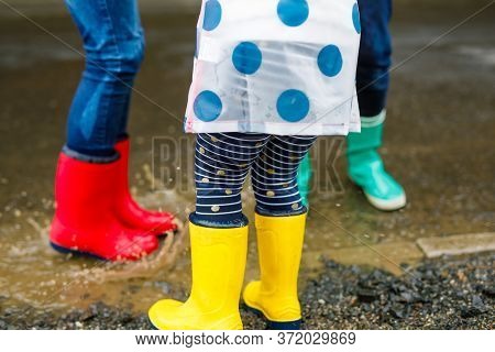 Close-up Of Three Children, Toddler Girl And Two Kids Boys Wearing Red, Yellow And Green Rain Boots 