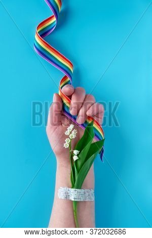 Rainbow Ribbon In Hand Of Mature Woman With Lily Of The Valley Flowers. Bouquet Attached With Medica