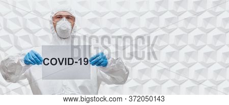 COVID-19 concept. A doctor in a protective suit holds a sign COVID-19 on a white background. Copy space.