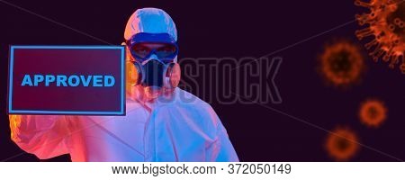 COVID-19 concept. A doctor in a protective suit holds a sign approved on the background of coronavirus. Copy space. 