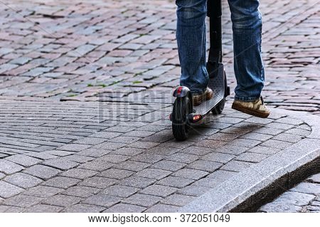 Riding E-scooter In Spring. Boy Rides An Electric Scooter On A City Street, Legs On A Sidewalk.