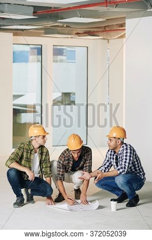 Vertical Shot Of Three Professional Engineers Sitting On Hunkers In Empty Room Of New Building Corre