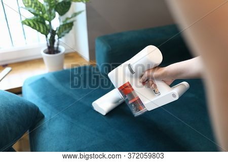 Close-up Of Womans Hand Cleaning Sofa With Small Electrical Compact Vacuum Cleaner. Stylish Seagreen