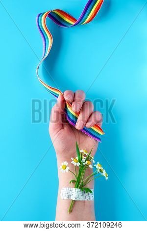 Rainbow Ribbon In Womans Hand With Chamomile Flowers And Grass Bouquet Attached With Medical Patch. 