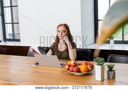 Focus Of Freelancer Holding Document Near Digital Devices, Credit Card And Fruits On Table