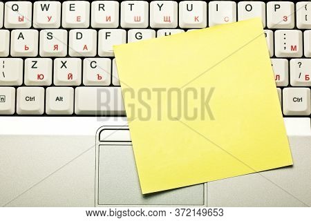 Top View Of A Blank Empty Clear Yellow Sticky Note On Grey Laptop Keyboard Trackpad.