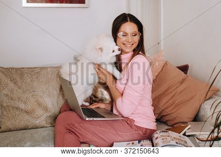 A Girl In Pajamas At Home Is Working On A Laptop With Her Dog Spitzer, The Dog And Its Owner Are Res