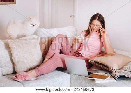 A Girl In Pajamas At Home Is Working On A Laptop With Her Dog Spitzer, The Dog And Its Owner Are Res