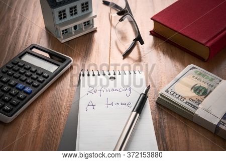 refinancing words on notebook with us dollars and stuff on wooden desk.