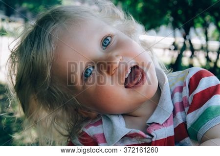 Portrait Of A Cute Happy Little Boy With Blond Hair And Blue Eyes, Whearing A Hat, Smiling And Playi