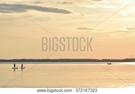 Paddling At Sunset In The Eckernförde Bay, In Northern Germany. The Dark Silhouette Of Two People On